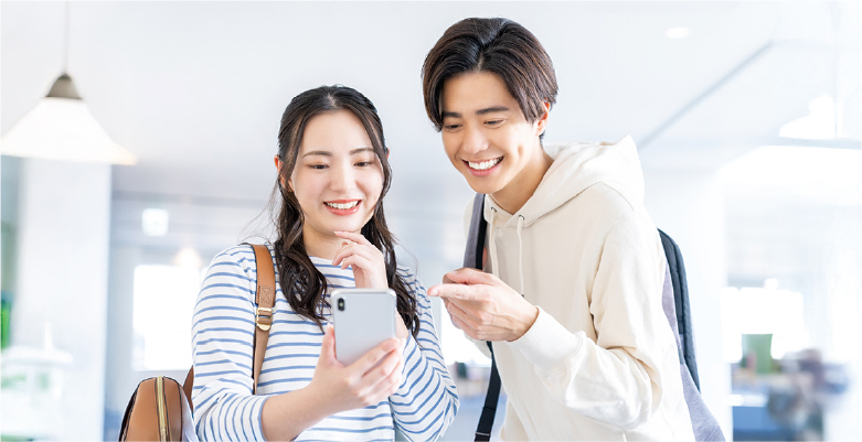 若い男女がスマートフォンを見ながら笑い合っている写真